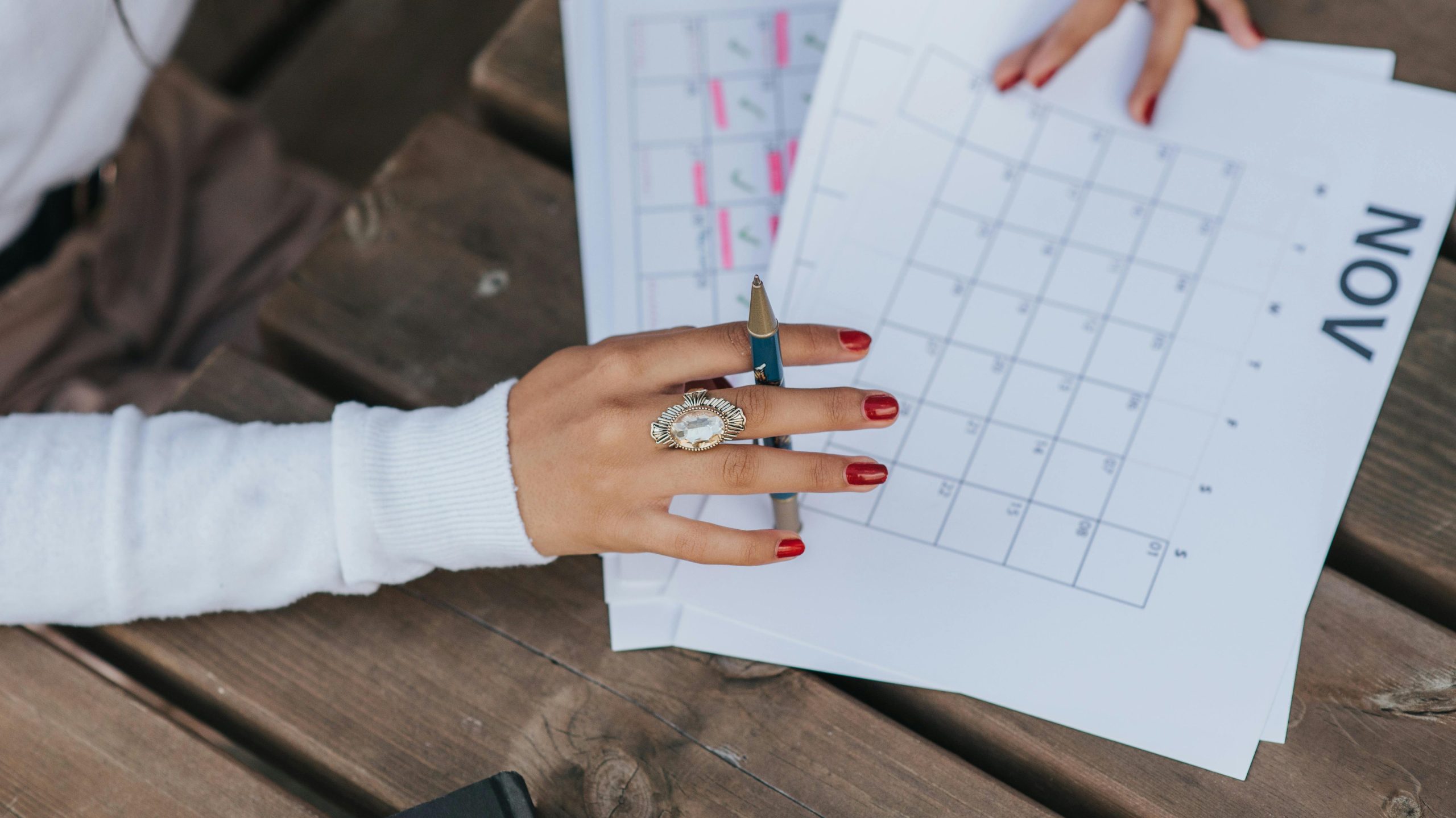 From above crop anonymous female in white blouse sitting at wooden table with pen and making list of plans for month