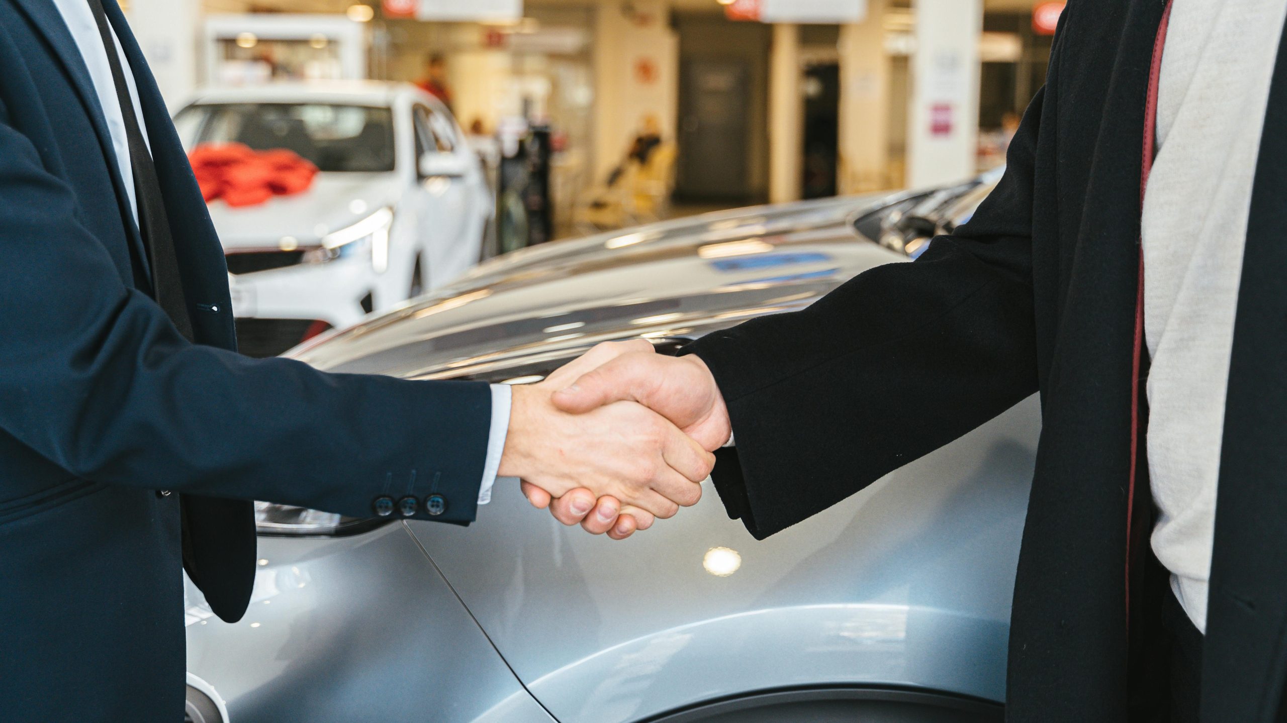 Two businessmen shaking hands in a car dealership, sealing a deal.