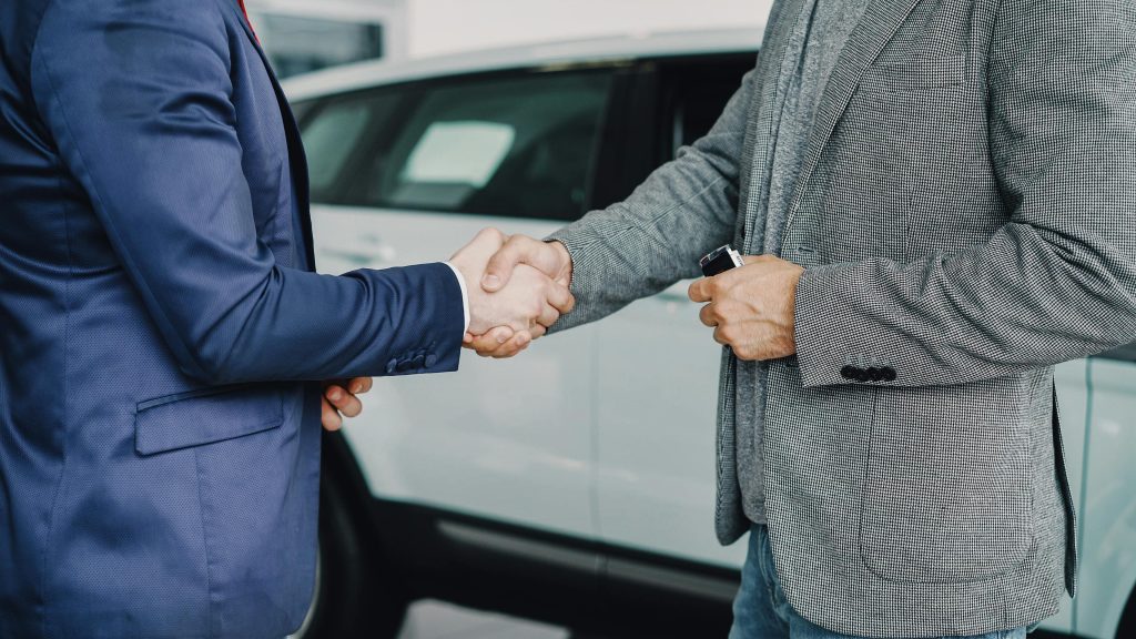 8 фрази, които силните дилърски оператори никога не казват 1 Two businessmen shaking hands in a car dealership, sealing a deal.