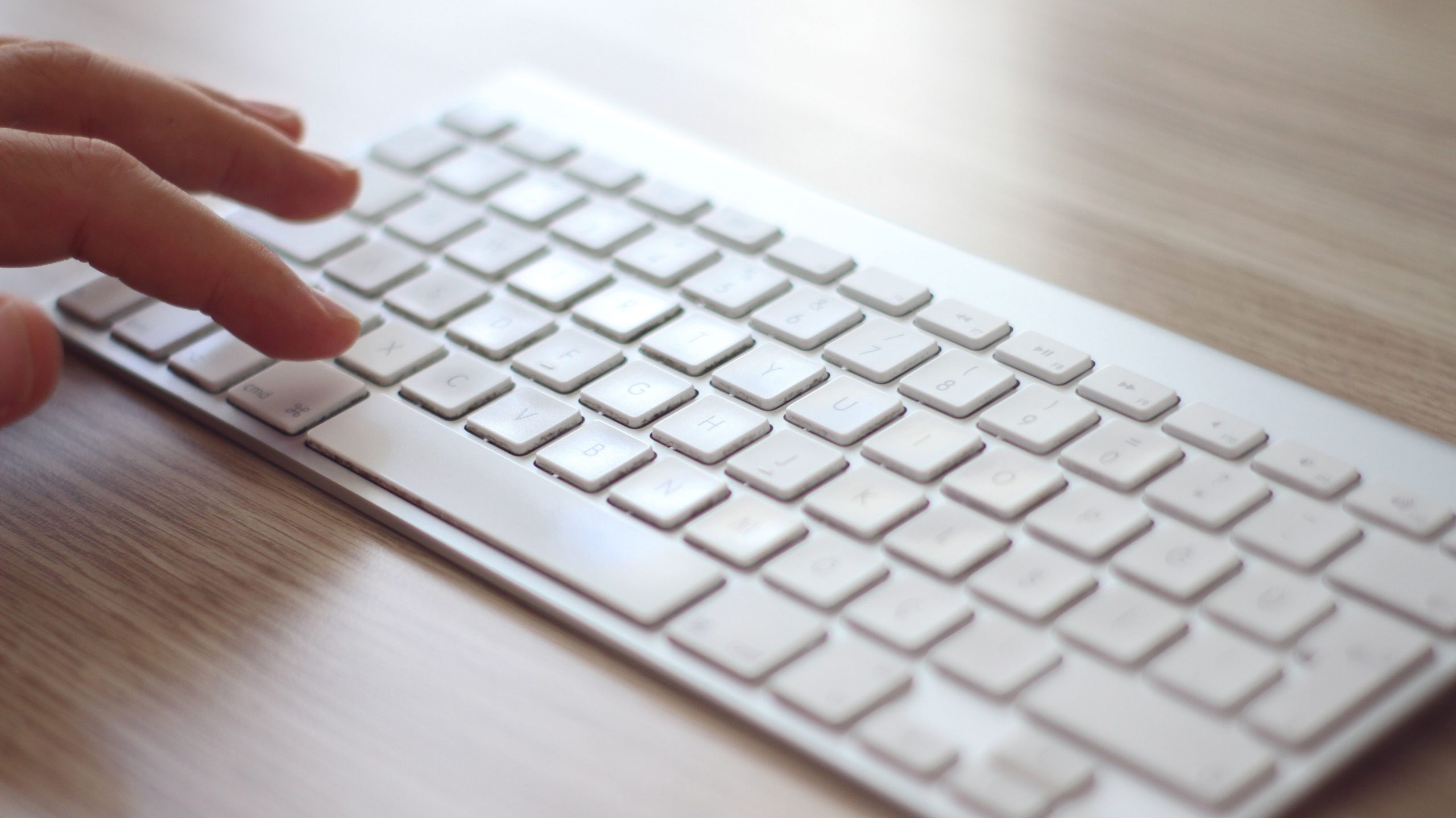 Close shot of a hand typing on a sleek white wireless keyboard, ideal for tech and blogging themes.